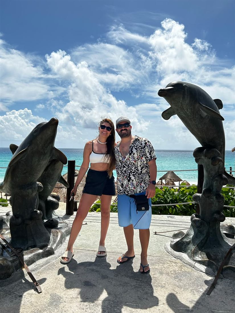Leonel y su pareja entre esculturas de delfines frente al mar de Cancún