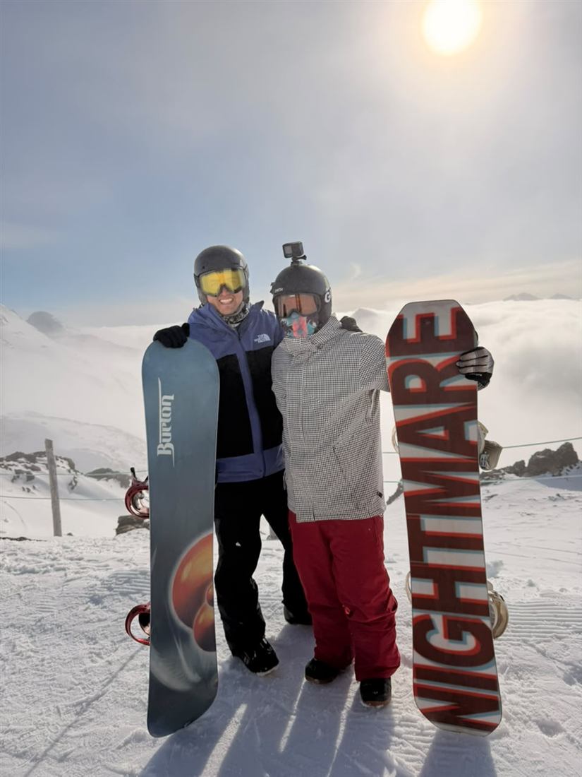 Dos viajeros con tablas de snowboard en la cima de una montaña nevada